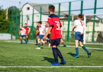 Obraz premium Boys in white and blue sportswear plays football on field, dribbles ball. Young soccer players with ball on green grass. Training, football, active lifestyle for kids concept 