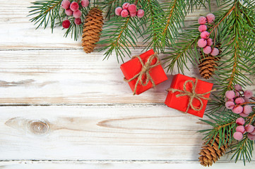 Christmas tree branches Christmas tree with cones red berries in the upper right corner and two red gift boxes on a white wooden background top view