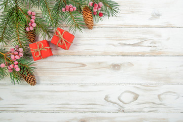 Christmas tree branches with cones red berries in the upper left corner of the image and two red gift boxes on a white wooden background top view