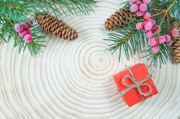Christmas tree branches with cones at the top of the image and a gift red box on a wooden disk close up