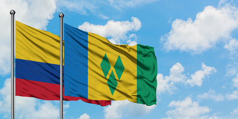 Colombia and Saint Vincent And The Grenadines flag waving in the wind against white cloudy blue sky...