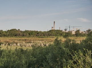 Obraz premium Paisaje de campiña con chimeneas fabriles a lo lejos, impacto en el medio ambiente.