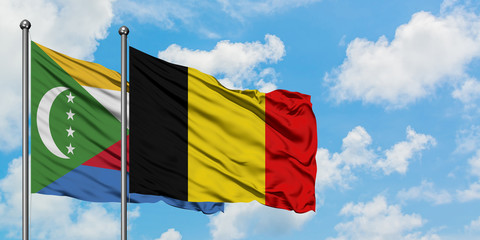 Comoros and Belgium flag waving in the wind against white cloudy blue sky together. Diplomacy...