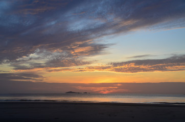 Dawn beauty, picturesque tropical orange coloured stratocumulus cloud coastal sunrise seascape in a blue sky.