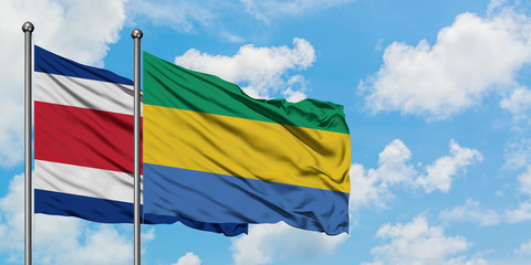 Costa Rica and Gabon flag waving in the wind against white cloudy blue sky together. Diplomacy...