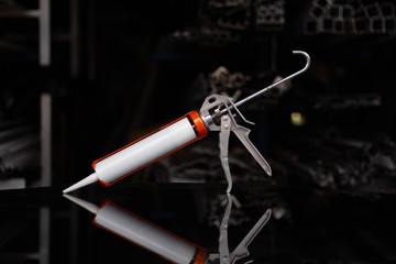 Caulking gun with a black silicon background.