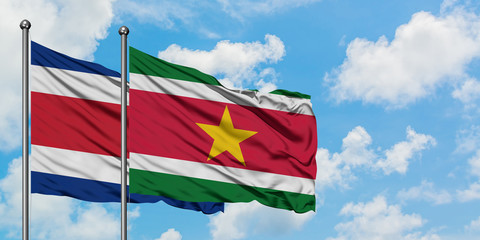 Costa Rica and Suriname flag waving in the wind against white cloudy blue sky together. Diplomacy concept, international relations.
