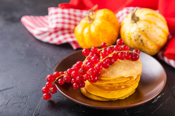 pumpkin pancakes with red currant in a plate on a table, selective focus, copy space