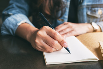 Closeup image of a woman writing on a blank notebook on the table - obrazy, fototapety, plakaty