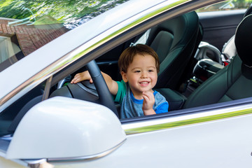 Toddler boy in playing in the drivers's seat of his family's car in sunglasses