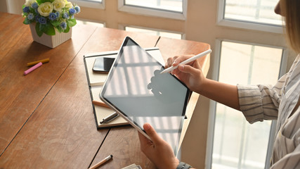 Female's using her tablet and stylus pen with creative project on wooden table.