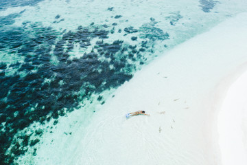 Woman snorkeling with many small sharks near white sand beach in turquoise clean water. Drone aerial view. Tropical background and travel concept