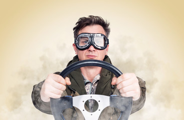 Cool man in stylish goggles with steering wheel, smoke around, yellow background. Front view. Car driver concept