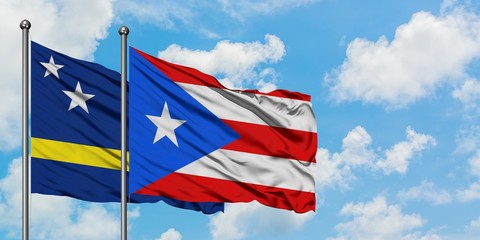 Curacao and Puerto Rico flag waving in the wind against white cloudy blue sky together. Diplomacy concept, international relations.
