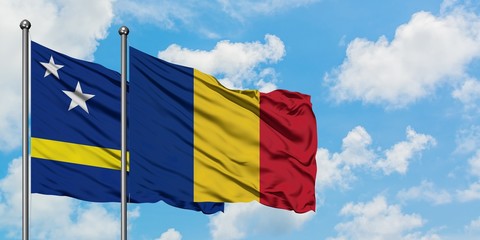 Curacao and Romania flag waving in the wind against white cloudy blue sky together. Diplomacy...
