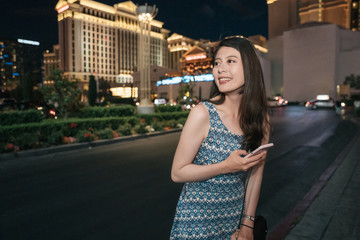 beautiful young college girl student in summer break trip in las vegas. happy lady traveler walk around night city and holding mobile phone using urban wifi. Modern technology and communication.