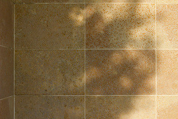 Natural stone tile wall texture background with tan color porous stone blocks, showing nearby tree shadows