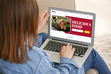 Fototapeta premium Young woman using laptop for ordering food at home