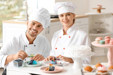 Young confectioners decorating tasty dessert in kitchen - obrazy, fototapety, plakaty