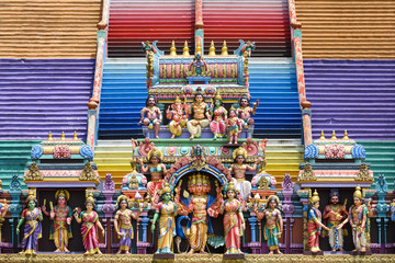 (Selective focus) Representation of Hindu gods in the foreground and a colorful stairs leading to the Batu Caves in the background. Kuala Lumpur, Malaysia