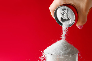 Pouring of sugar from can into glass on color background