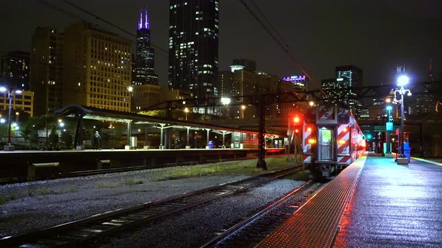 Metra train leaves station/platform to reveal skyline in downtown Chicago at night