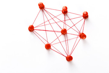 Network with red pins and string,  linked together with string on a white background suggesting a...
