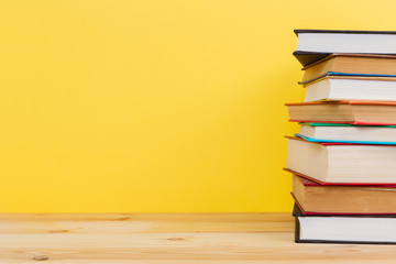 Simple composition of many hardback books, raw of books on wooden table and pastel yellow background