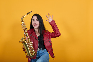 Crazy smiling young woman in casual clothes, keeping saxophone, showing palms over isolated on...