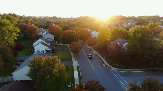 Pick up truck turns onto street through residential neighborhood community, colorful autumn fall leaves line the road, evening glow or warm sunset