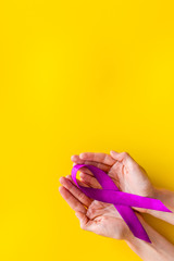 Lilac ribbon in hands is symbol of Alzheimers disease on yellow background top view space for text