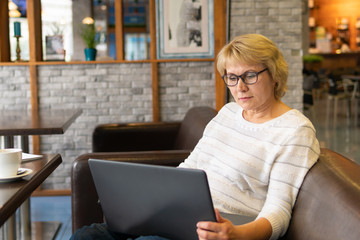 A woman with a laptop works in a cafe, she watches social networks.