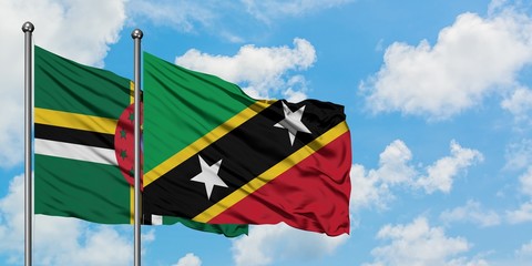 Dominica and Saint Kitts And Nevis flag waving in the wind against white cloudy blue sky together. Diplomacy concept, international relations.