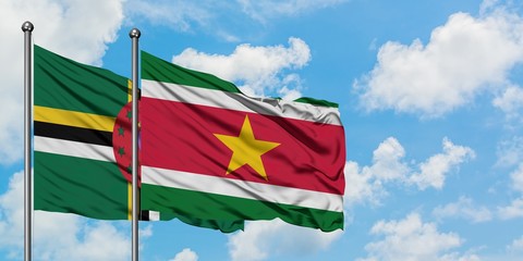 Dominica and Suriname flag waving in the wind against white cloudy blue sky together. Diplomacy concept, international relations.