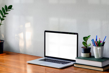 Workspace with laptop computer, book and houseplant on wooden table white concrete wall.