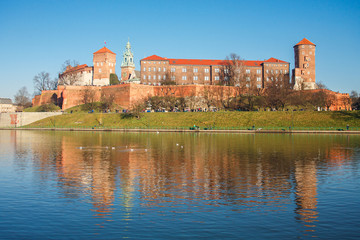 Fototapeta na wymiar The view of Wawel castle in Krakow city with reflection in the water, ducks floating on the foreground, group of tourist walking around castle in sunny winter day