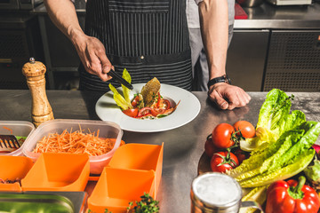 Professional chef cooking in the kitchen restaurant at the hotel, preparing dinner. A cook in an apron makes a salad of vegetables and pizza.