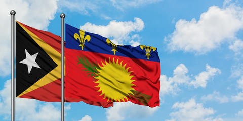 East Timor and Guadeloupe flag waving in the wind against white cloudy blue sky together. Diplomacy concept, international relations.