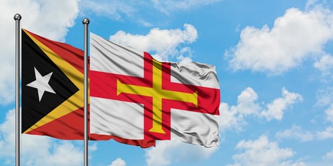 East Timor and Guernsey flag waving in the wind against white cloudy blue sky together. Diplomacy concept, international relations.