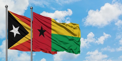 East Timor and Guinea Bissau flag waving in the wind against white cloudy blue sky together. Diplomacy concept, international relations.