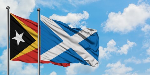 East Timor and Scotland flag waving in the wind against white cloudy blue sky together. Diplomacy concept, international relations.