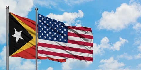 East Timor and United States flag waving in the wind against white cloudy blue sky together. Diplomacy concept, international relations.