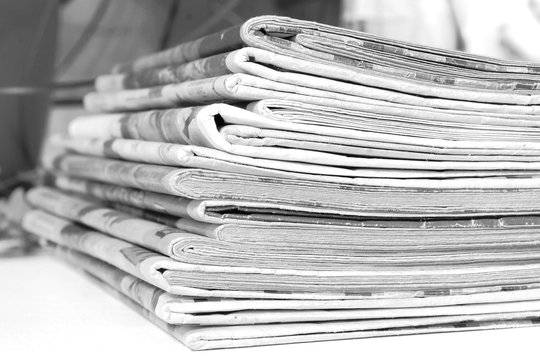 Pile of fresh morning newspapers on the table at office. Latest financial and business news in daily paper. Pages with information (headlines, articles, photos, text). Folded and stacked journals    