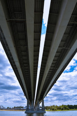 Large bridge over the river, view from below. On the background of contrasting clouds and blue sky.