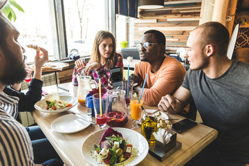 A company of multicultural  young people in a cafe eating pizza, drinking cocktails, having fun