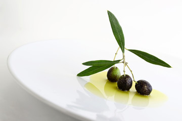 Foglie verdi delle olive fresche su un piatto bianco isolato su fondo bianco.