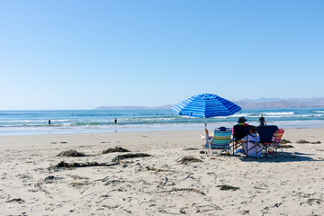 People sitting under bright blue striped umbrella