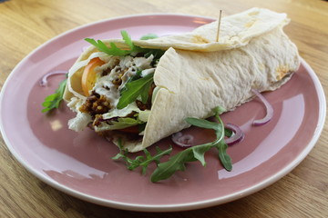 Delicious beef burrito with salad and cheese on a white plate.