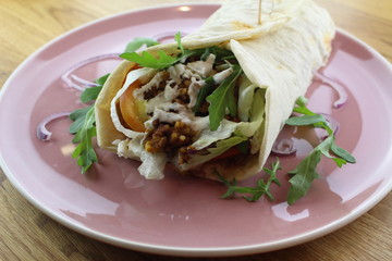 Delicious beef burrito with salad and cheese on a white plate.