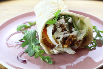 Delicious beef burrito with salad and cheese on a white plate.